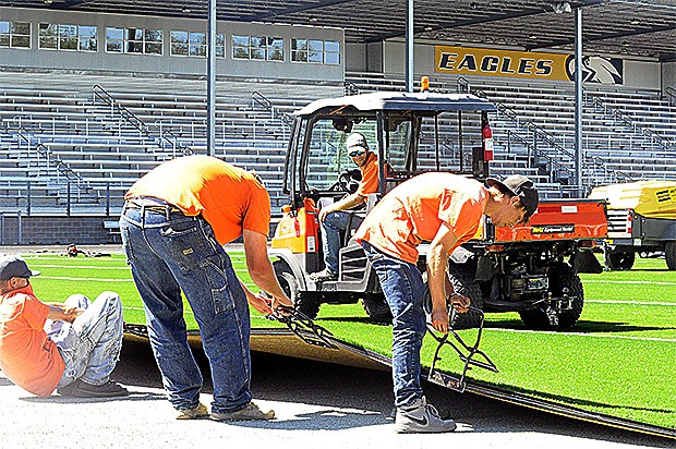 Workers stretch out the new turf in Arlington. A $200