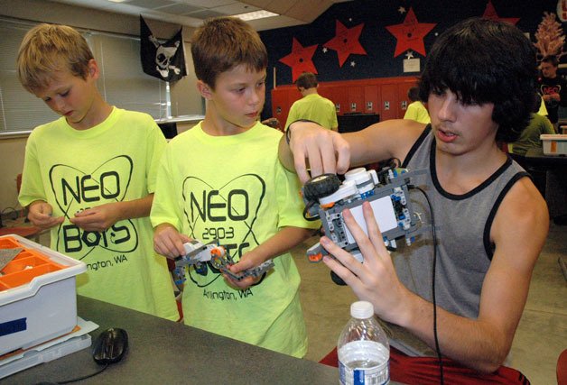 Kirk Boxleitner/Staff Photo Arlington fourth-graders Braden Dahlgren and Zack Davis work with Arlington High School senior and NeoBots Team member John Allen on preparing their robot for its final competition during the July 17 summer robotics day camp.