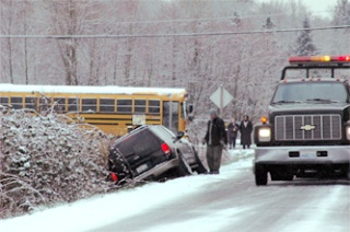 A school bus and several cars wait patiently while a tow truck removes a vehicle from the ditch on 67th Avenue Monday morning. The slush on the road had transitioned to a patch of ice in that location.